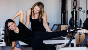 A smiling client on a Pilates reformer receiving hands-on instruction from a Right Balance Pilates instructor