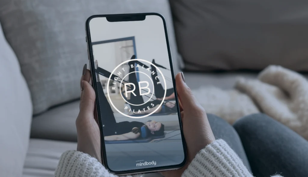 Woman holding a phone displaying the Right Balance Pilates App load screen